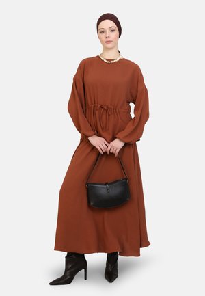 Long brown dress with long sleeves and a drawstring waist, paired with black handbag and high-heeled boots. Textured fabric.