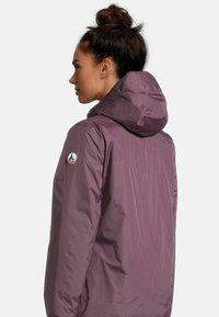 Giacca impermeabile viola con cappuccio, con un logo sul retro e una toppa sul braccio. Il tessuto è liscio e leggero.