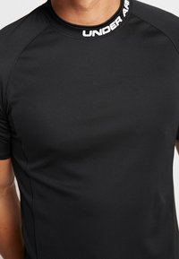 Svart åtsittande träningsskjorta med korta ärmar, tillverkad av slätt tyg. Har en hög krage med "UNDER ARMOUR"-logotypen i vitt.