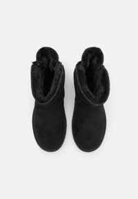 Černé kotníkové boty s měkkou kožešinovou podšívkou, materiál připomínající nubuk a prošívané detaily kolem vršku, s designem zaoblené špičky.