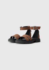 Sandales en cuir marron au design minimaliste, avec deux brides horizontales et une bride de cheville maintenue par une boucle en métal. Semelle extérieure noire.