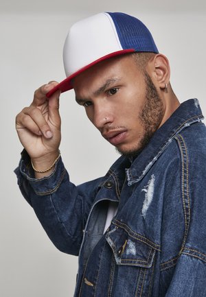 Casquette snapback rouge, blanche et bleue avec un avant rigide, un dos en mesh et une visière plate, portée avec une veste en denim usée.
