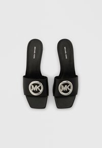Czarne klapki na płaskiej podeszwie z szerokim paskiem ozdobionym srebrnym okrągłym logo oraz prostokątnym otwartym przodem. Gładka skórzana faktura.