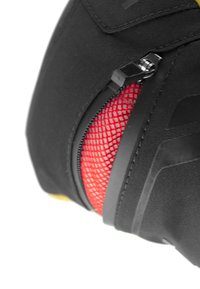 Zaino nero con dettaglio in rete rossa testurizzata vicino a una cerniera, realizzato in tessuto liscio, materiali a contrasto e un design strutturato.