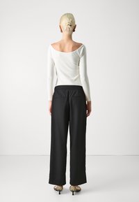 Langarm, off-shoulder wit top gecombineerd met losse zwarte broeken en gepatternde hakken. Zachte stof met een ontspannen pasvorm en subtiele details aan de achterkant.