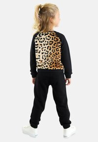 Schwarze Jogginghose kombiniert mit einem schwarzen Langarmoberteil mit einem Leopardenmuster auf dem Rücken. Weicher Stoff mit gerippten Bündchen und Saum.