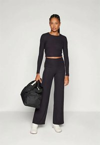 Svart ribbet crop top og høyt liv flared bukser, kombinert med en svart duffel bag og hvite sportsko. Jevn tekstur, tettsittende design.