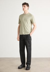 Lys grøn kortærmet skjorte med rund hals, parret med løse sorte denimbukser med synlige sømme og store forlommer.