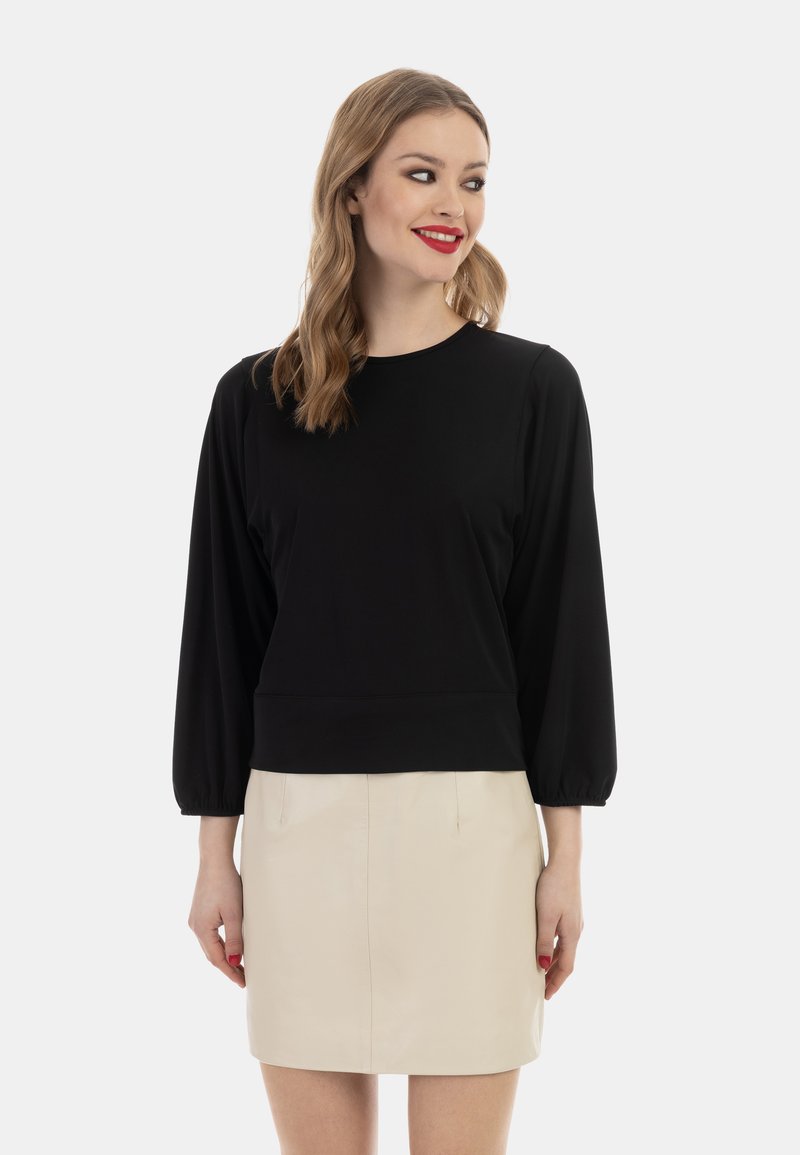Sort langærmet top med rund hals, der har en tætsiddende silhuet og gathered ærmer. Parret med en lys beige, knælang nederdel.