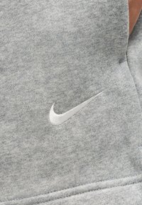 Κοντινή λήψη γκρι υφάσματος με λευκό κεντητό λογότυπο Nike swoosh σε ένα κομμάτι ρούχου.