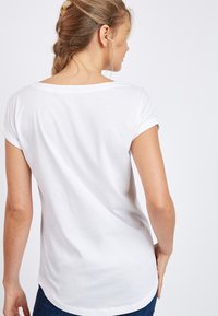 Witte katoenen T-shirt met een ronde halslijn en omgeslagen korte mouwen, met een licht gebogen zoom aan de achterkant. Soepele textuur.