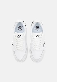 White sneakers featuring a smooth leather upper, round toe, and black logo accents. Lace-up design with a cushioned collar and tongue.