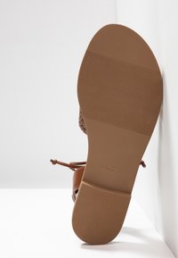 Semelle d'une sandale marron avec une adhérence texturée et la marque "ALDO", montrant un talon plat et des brides en cuir tressé.