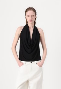 Mustat halterneck-topit, joissa on roikkuva etuosa, valmistettu pehmeästä kankaasta. Yhdistetty korkeavyötäröisten valkoisten housujen kanssa, joissa on taskut ja löysä istuvuus.