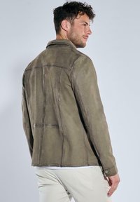 Olivgrüne Lederjacke mit strukturiertem Design, sichtbaren Nähten und klassischem Kragen. Sie hat eine leicht abgenutzte Textur.
