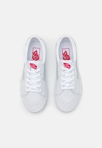 Sneaker bianche con tomaia in pelle liscia, punta tonda, dettagli perforati, lacci bianchi e un logo Vans rosso sulla soletta.