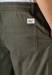 Pantalones cortos verde oliva fabricados con un material duradero, que cuentan con un bolsillo trasero con una etiqueta cuadrada y una cinturilla elástica para un ajuste cómodo.