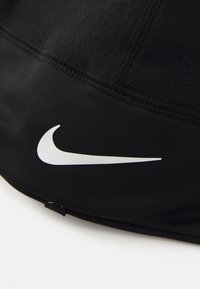 Svart sportig keps med en slät yta, som har en framträdande vit Nike swoosh-logotyp. Stickningsdetaljer synliga längs sömmarna.