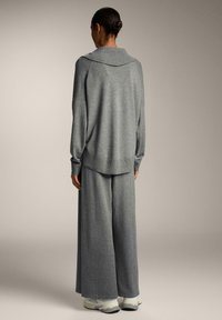 Maglione grigio di grandi dimensioni con colletto ampio, abbinato a pantaloni a gamba larga coordinati. Tessuto morbido, design informale, con evidenti dettagli a coste ai polsini.