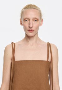 Top in lino marrone senza maniche con scollatura quadrata e spalline sottili e regolabili, caratterizzato da un tessuto testurizzato e un design minimalista.