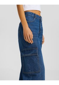 Pantalones cargo de denim azul con bolsillos laterales, una cintura de altura media y detalles de costura visibles. Textura suave y corte relajado.