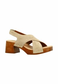 Beige suède sandaal met een kruisbandontwerp, houten blokhak en decoratieve metalen studs op de banden. Open teen, slingback stijl.