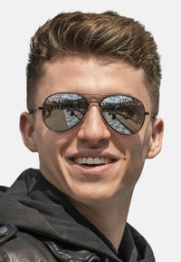 Black round sunglasses with reflective lenses, set in thin metal frames. Dark hair, light skin, wearing a black hoodie and leather jacket.