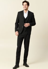 Traje negro de tres piezas con corte ajustado, que presenta una tela texturizada, solapas con muesca y una chaqueta de un solo botón. Combinado con zapatos negros.