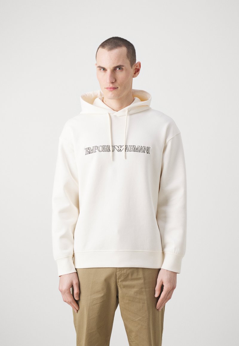Felpa bianca in cotone con logo frontale, cappuccio con cordino, polsini a coste e vestibilità rilassata, abbinata a pantaloni khaki.