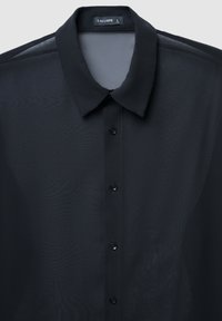 Schwarzes transparentes Hemd mit klassischem Kragen, ausgestattet mit einem strukturierten Stoff und sechs schwarzen Knöpfen an der Vorderseite. Markenlabel sichtbar.