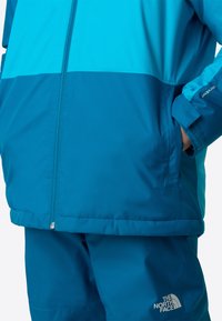 Jachetă albastră rezistentă la apă cu design color-block, prevăzută cu fermoar frontal, manșete ajustabile și buzunare laterale.