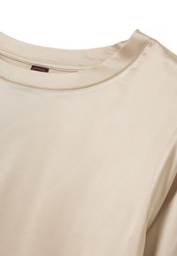 Camicia beige a maniche corte con una texture liscia simile alla seta e un collo rotondo. Presenta cuciture pulite e nessuna stampa o motivo visibile.
