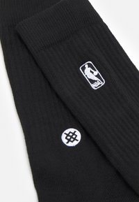 Calcetines de baloncesto negros fabricados en material acanalado, con el logotipo de la NBA bordado en blanco y un logotipo circular con un diseño de hashtag.