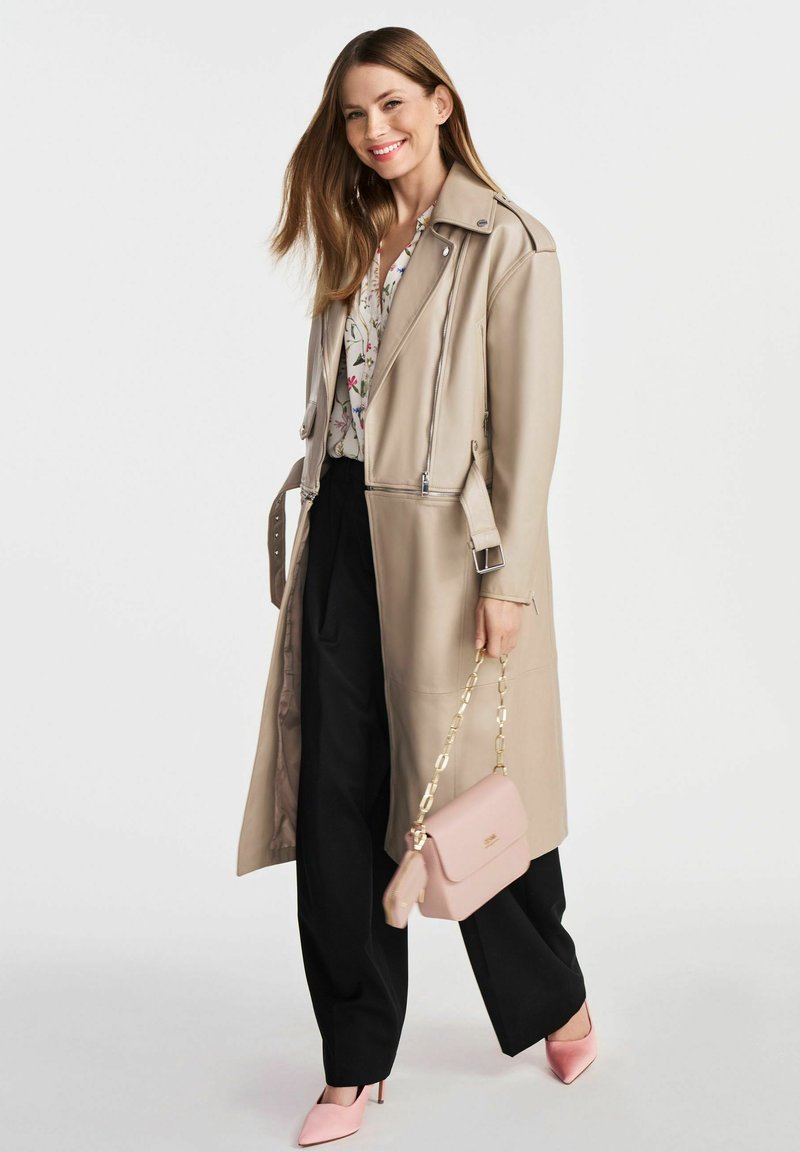 Beżowy długi płaszcz trench z srebrnymi zamkami, kwiecista bluzka, czarne szerokie spodnie, różowa torebka i dopasowane różowe szpilki.