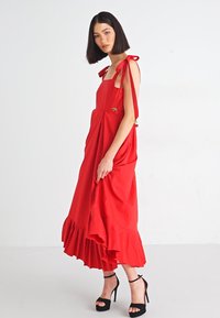 Red maxi dress with ruffled hem, bow straps, and side pockets. Made from lightweight fabric, features a relaxed fit and gathered detailing.