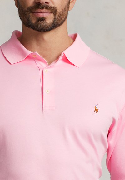 Šviesiai rožinė medvilninė polo marškinėliai su klasikiniu apykakle ir trijų mygtukų saga, kairėje krūtinės pusėje siuvinėtu logotipu.