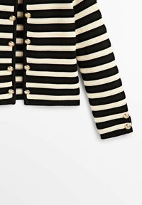 Cardigan en maille rayé horizontal noir et beige avec des boutons dorés sur le devant et aux poignets, présenté partiellement sur un fond blanc.