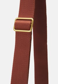 Sangle en tissu marron avec une texture côtelée, équipée d'une boucle rectangulaire en métal doré. La sangle semble robuste et adaptée à divers usages.