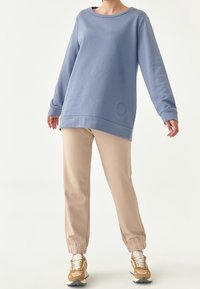 Helles blaues Sweatshirt mit rundem Ausschnitt und langen Ärmeln, kombiniert mit beigen, schmal zulaufenden Hosen und beige-weißen Sneakers.