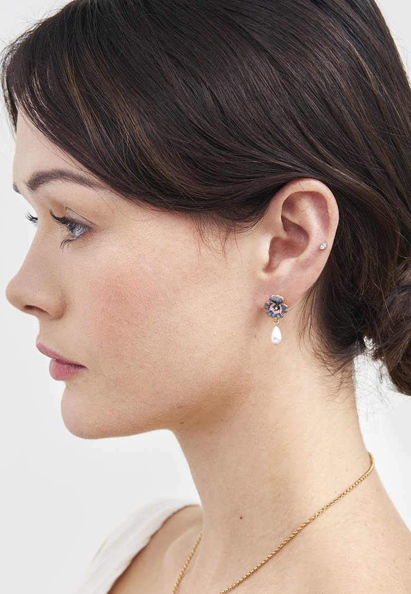 Young woman with dark hair wearing a floral earring with a hanging pearl and small stud on left ear, and a gold necklace.
