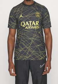 Maglia nera con linee geometriche gialle, con il logo Jordan e la scritta "Qatar Airways" ben visibili. Maniche corte, scollo rotondo.