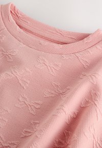 Maglione rosa con texture caratterizzato da un sottile motivo intrecciato a fiocchi, scollatura a coste e tessuto morbido e accogliente.