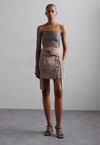 Strapless gray top with front buttons paired with a beige wrap skirt featuring double-breasted detail and side slit, worn with black heeled sandals.