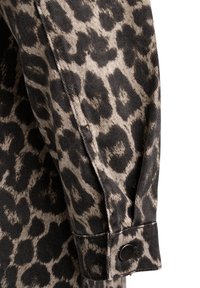 Poignet de manche longue en tissu imprimé léopard noir et beige avec fermeture à boutons-pression noirs.