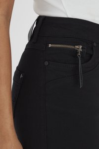 Jeans de mezclilla negra con cintura alta, bolsillo con cremallera frontal y costuras laterales que añaden un toque estructurado. El material parece suave y duradero.