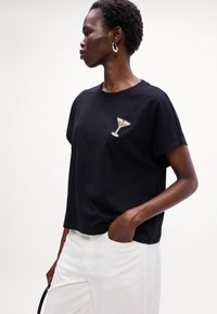 Sort bomulds t-shirt med korte ærmer og en afslappet pasform, der har et applikationsdesign af et cocktailglas med palietter på venstre bryst.