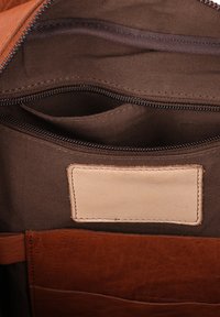 Ruskea nahkalaukku, jonka sisällä on vetoketjullinen tasku, sileä pinta, beige etiketti ja useita lokeroita järjestämistä varten.