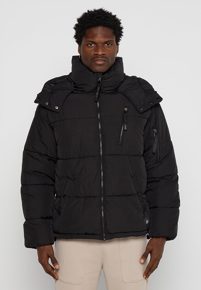 Czarna puchowa kurtka z wysokim kołnierzem, poziomym pikowaniem, podwójnymi kieszeniami na zamek i guzikami zatrzaskowymi na ramionach.