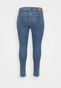 Jeans ajustados en denim azul claro, con una cintura de altura media, dos bolsillos traseros con detalles de costura y un parche de cuero marrón de la marca.