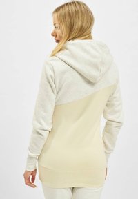 Hoodie mit langen Ärmeln in hellbeige und crème, mit einem gesprenkelten Muster, lässigem Schnitt und weicher Textur.